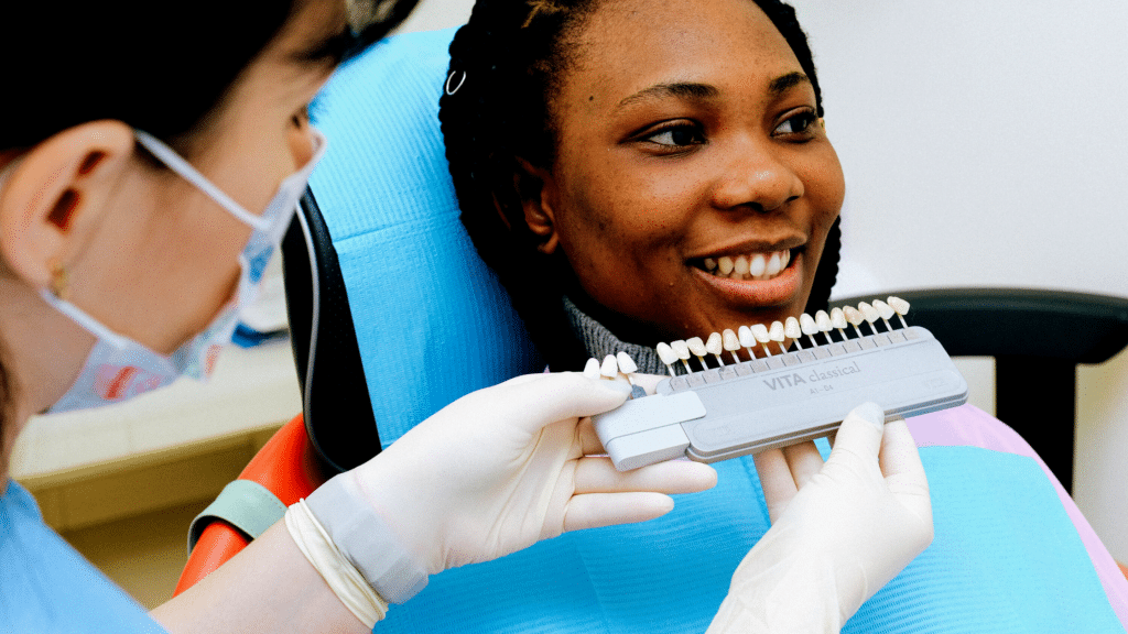 Dental professional showing tooth shade guide to smiling patient during consultation at dental office.