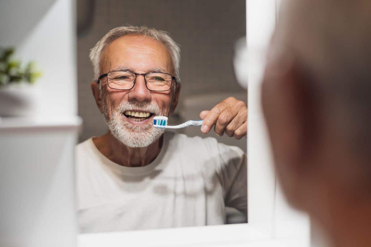 Senior brushing teeth after gum disease treatment to maintain healthy gums before dental implants